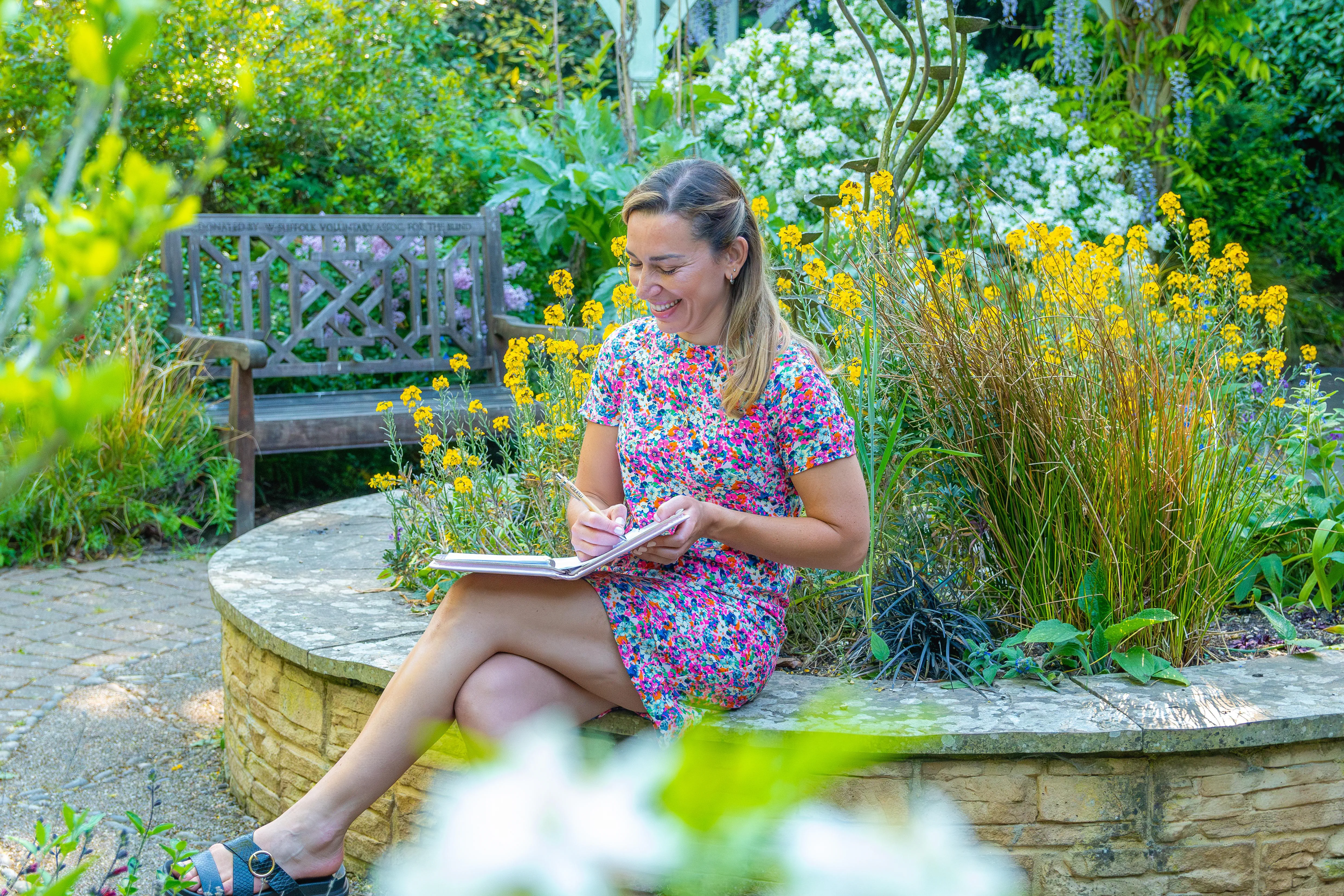A female businesswoman in a colourful dress making notes in a garden